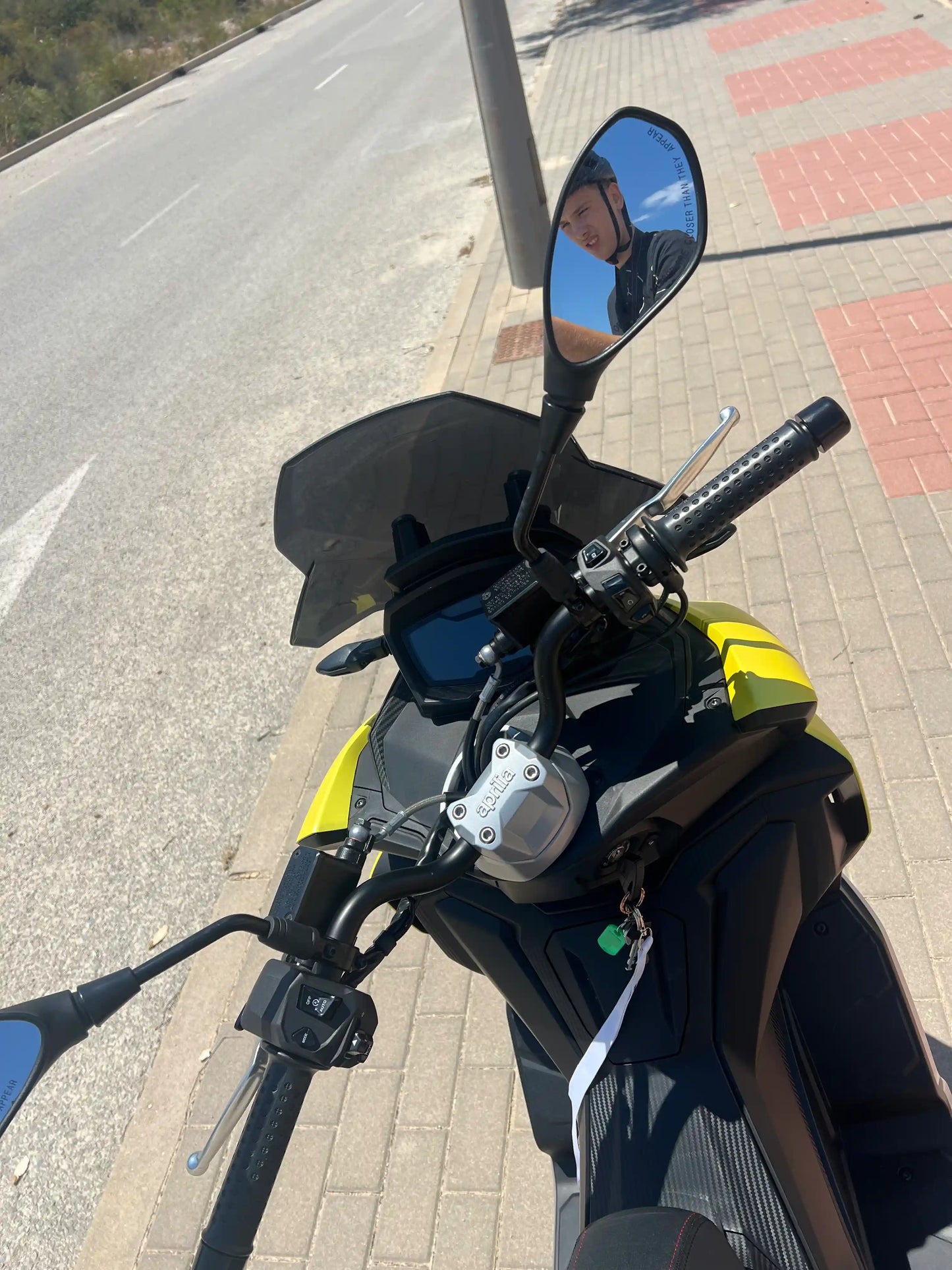 Yellow 2025 Aprilia SR GT 125 scooter instrument cluster, streeting and mirrors. Pictured on side walk in Spain