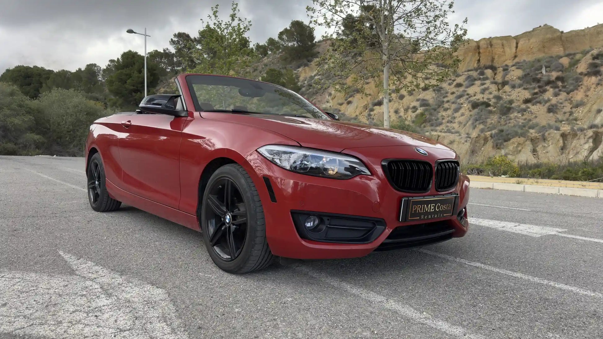 Red BMW 2 Series Convertible front right side on the street in Spain surrounded by trees