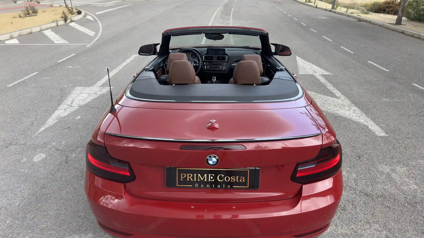 Red BMW 2 Series Convertible back with roof down on empty street in Spain