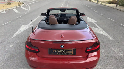 Red BMW 2 Series Convertible back with roof down on empty street in Spain