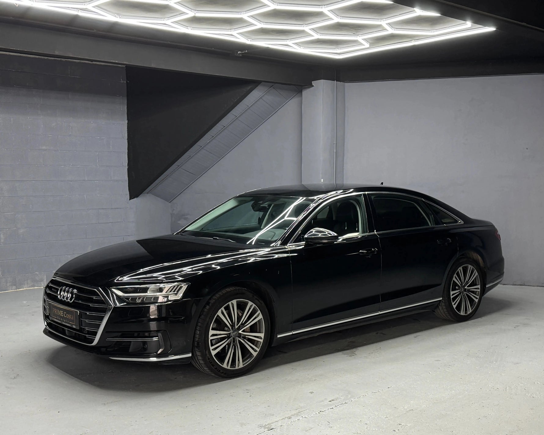 2019 Black Audi A8 Long front left side view, visible headlight and bumper, picture made in garage under hexagon lights