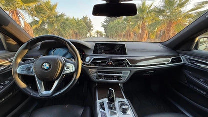 BMW 730D black leather interior and dashboard with steering wheel and palm trees behind windsheeld