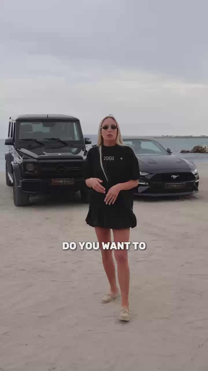 Good looking blonde girl stands behind luxury cars and explains where to rent them